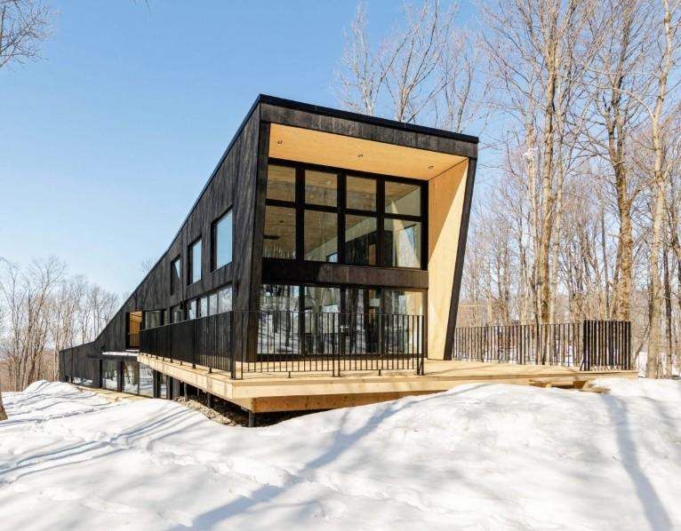 Modern dark-clad residence with expansive windows in a snowy wooded setting
