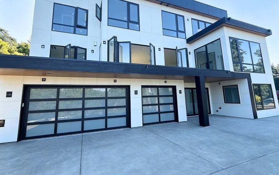 Full view of a three-story modern home with black impact windows, glass garage doors, and entry glazing